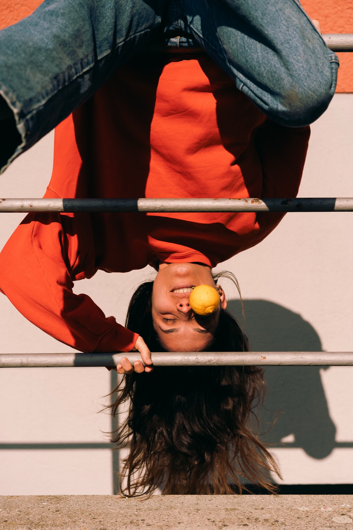 Cinzia hanging upside down from a railing, a lemon on her nose